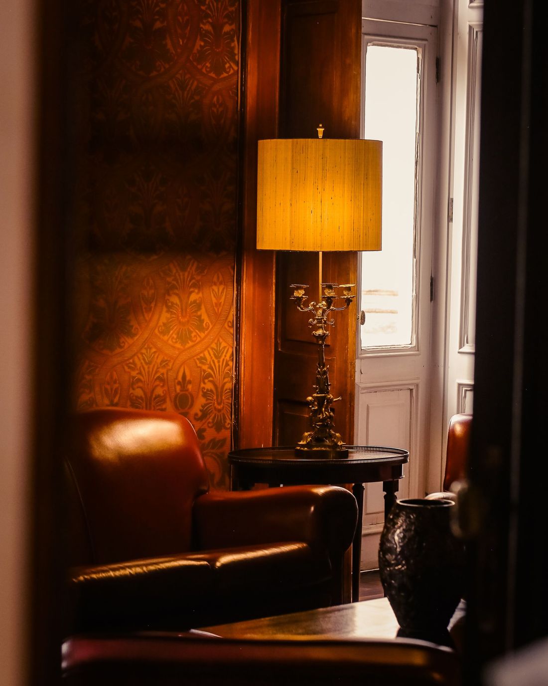 Living room with brown damask wallpaper, a leather armchair and a table lamp