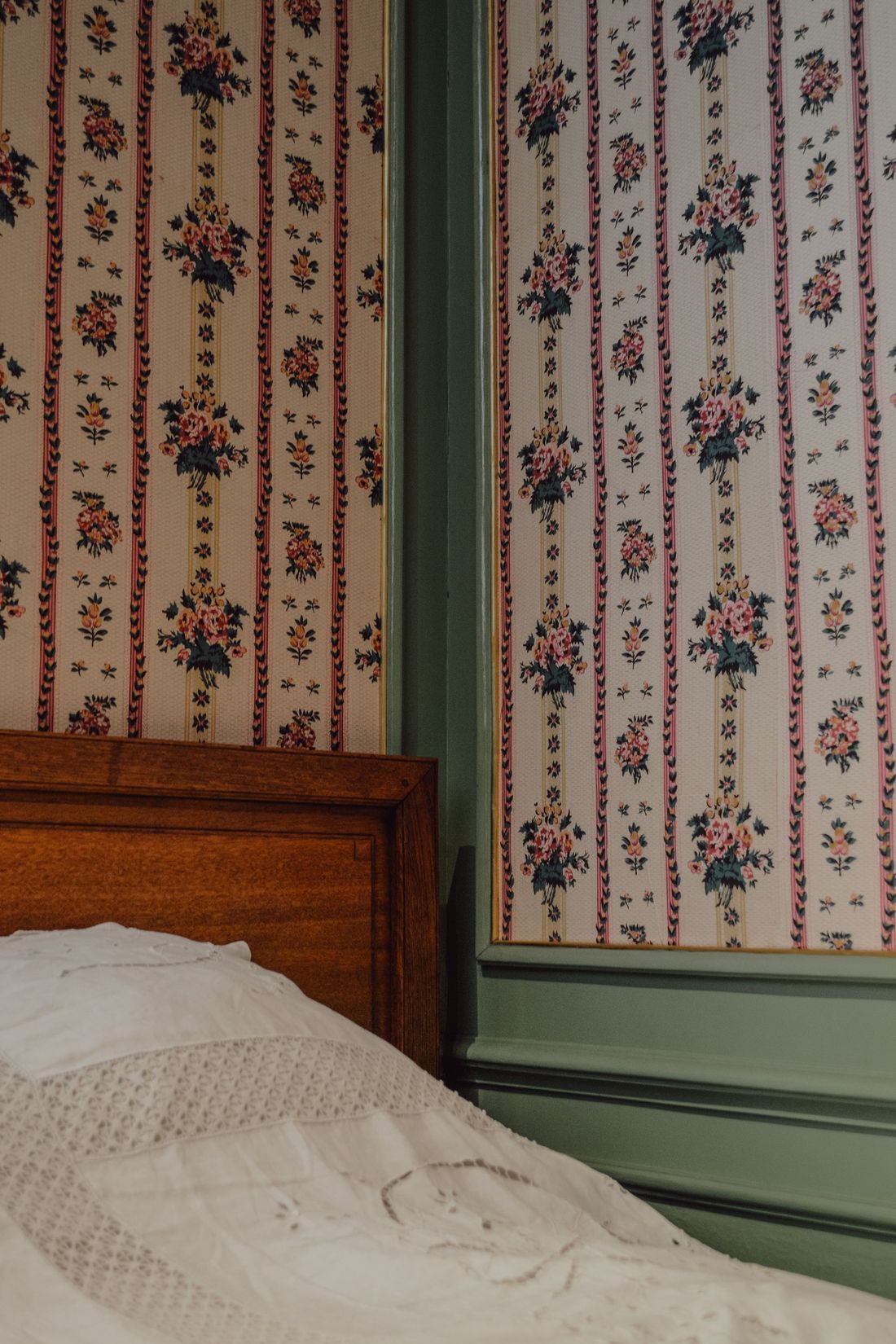 Vintage bedroom corner with striped floral wallpaper and a wooden bed
