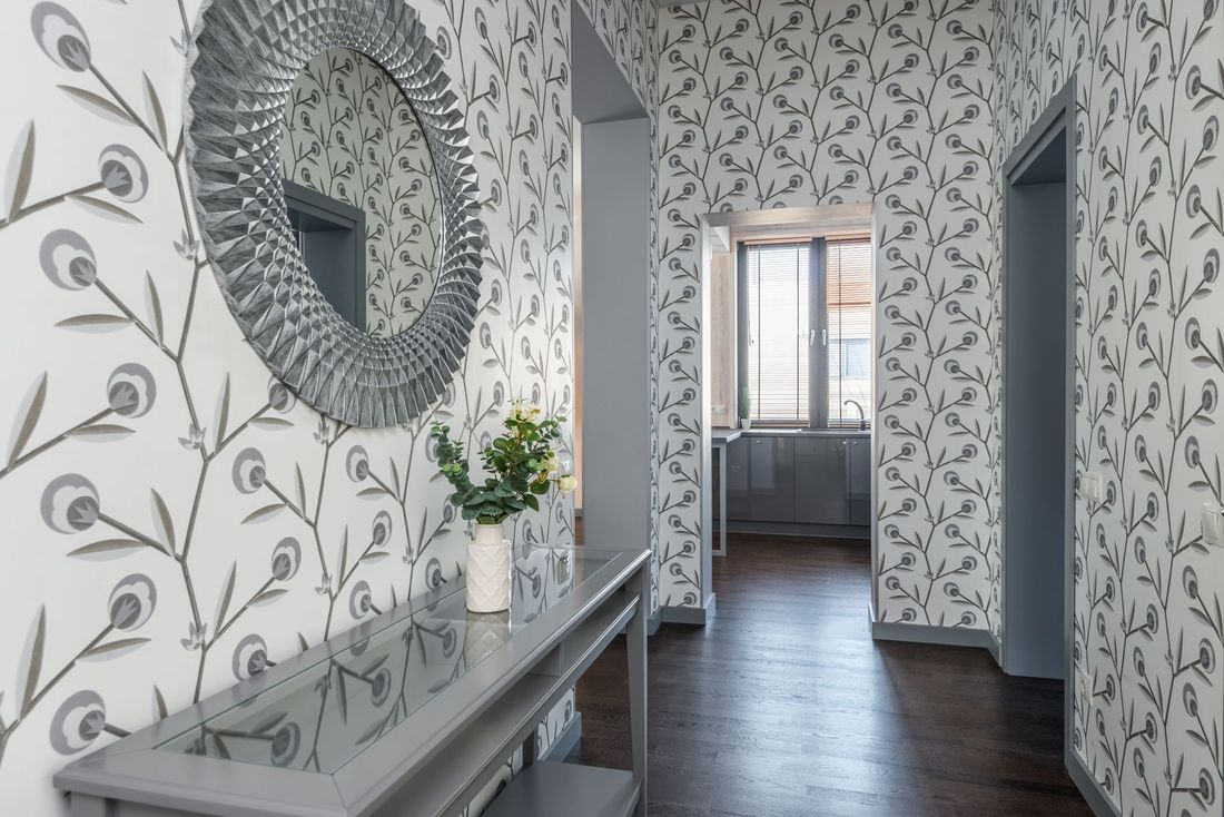 Hallway lined with peacock-motif wallpaper, a console table and round mirror