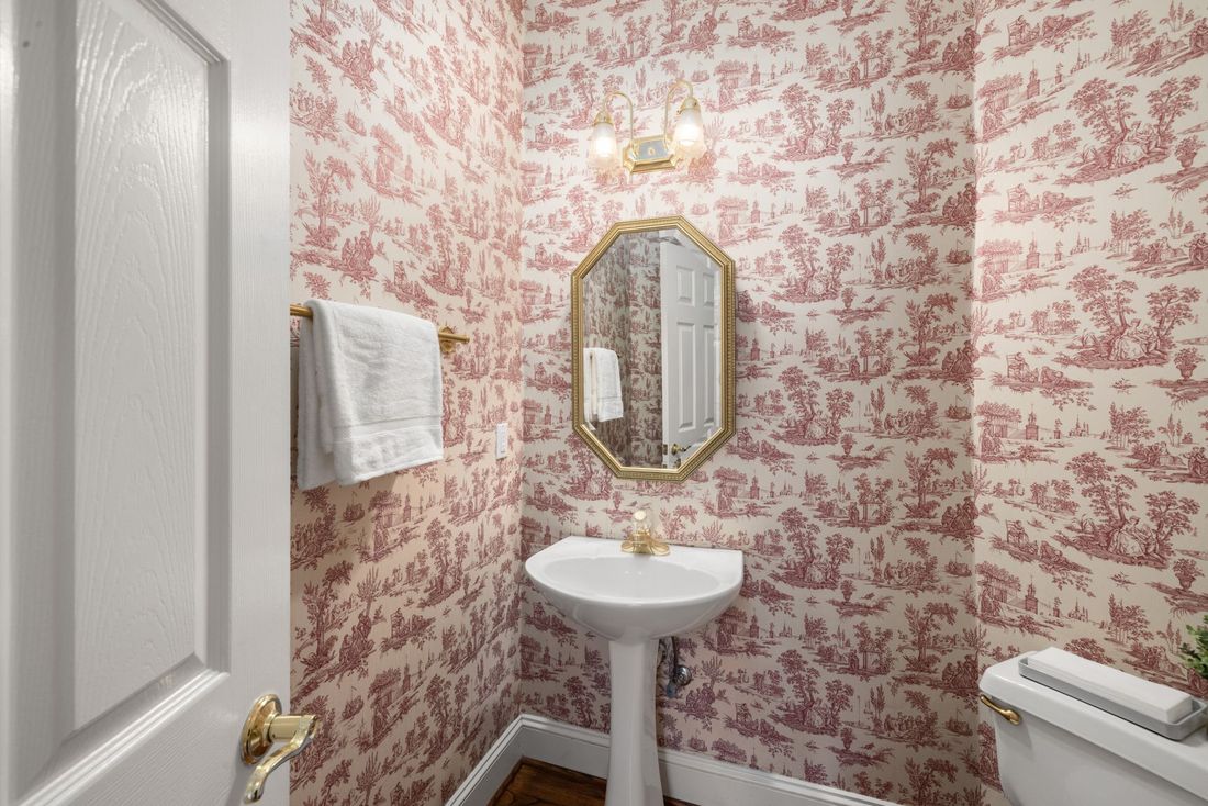 Powder room wrapped in red toile wallpaper with a pedestal sink