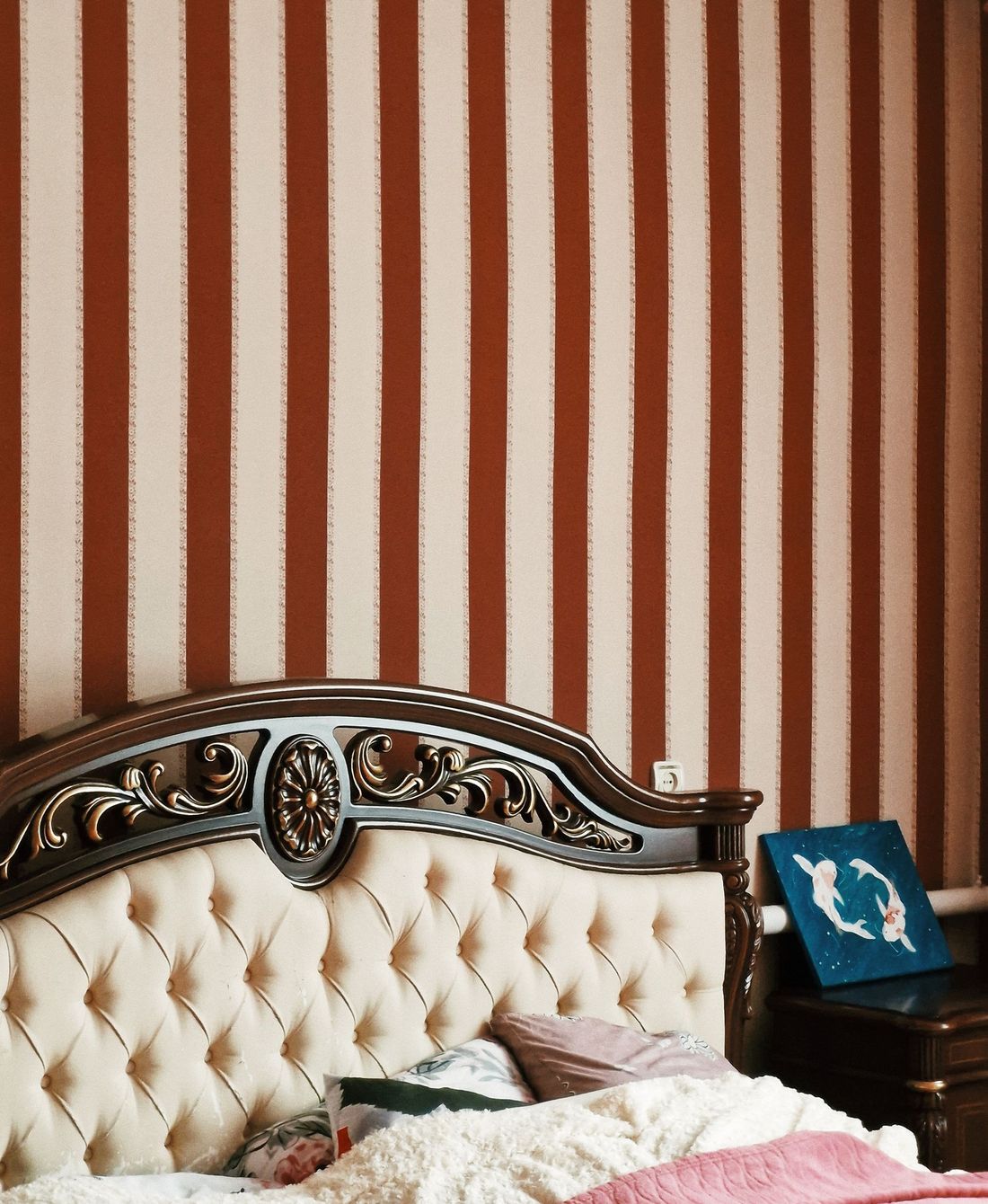 Bedroom with a striped statement wall behind a carved, tufted headboard