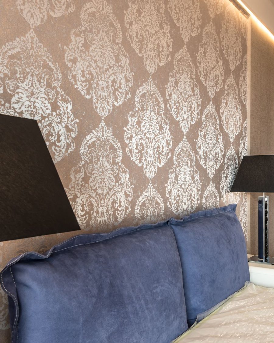 Bedroom with soft taupe damask wallpaper behind an upholstered bed