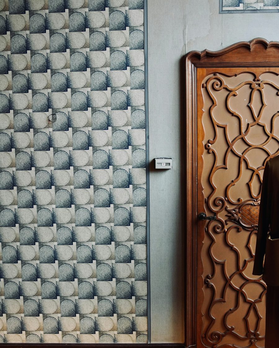 Teal scalloped wallpaper meeting a carved wooden door with precise pattern alignment